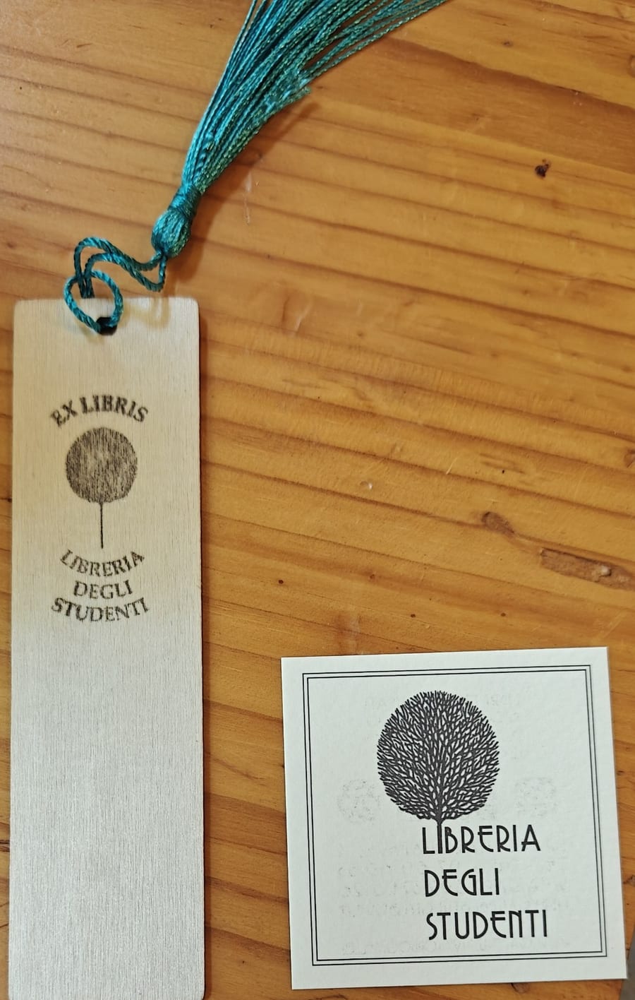 Il segnalibro in legno con il fiocco verde e il cartoncino ex libris della libreria, sul banco.